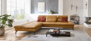 Großes Ecksofa aus cognacfarbenem Leder mit roten Kissen, modernes Wohnzimmer mit heller Fensterfront, Couchtisch und urbaner Einrichtung.